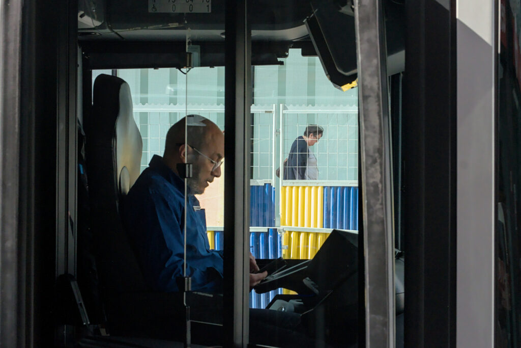 A man sits inside a public bus, focused on his laptop, surrounded by soft reflections on the window.