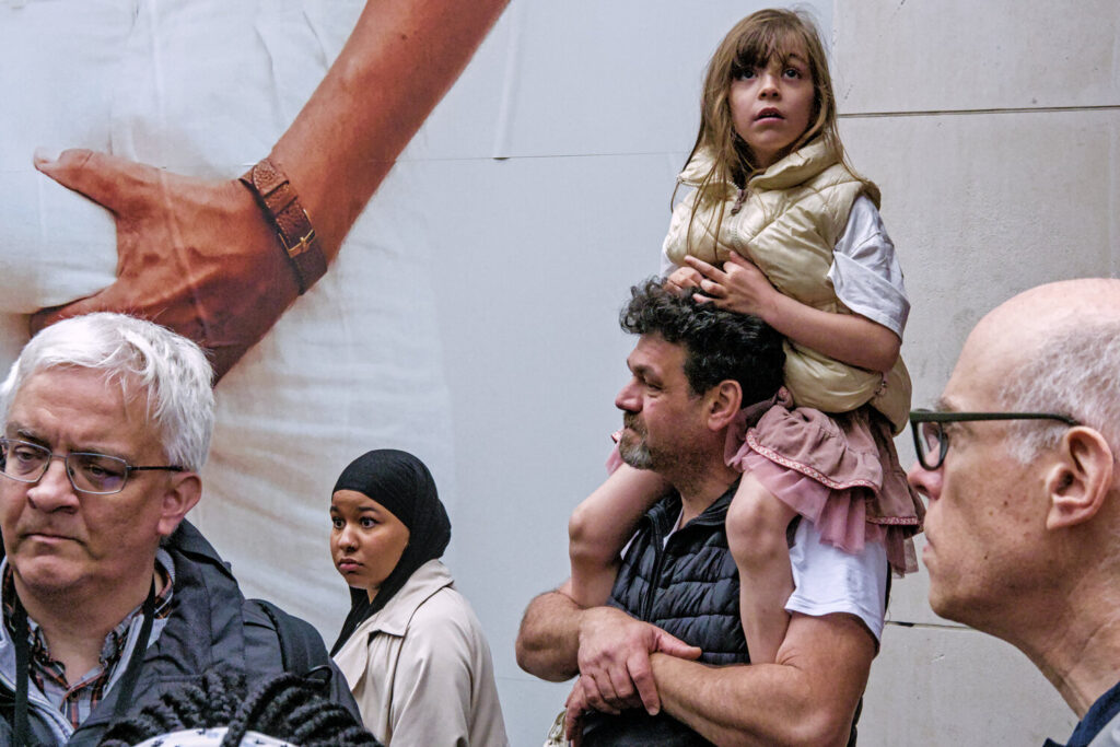 A little girl on the shoulders of her father. Other people passing by and looking in different directions.