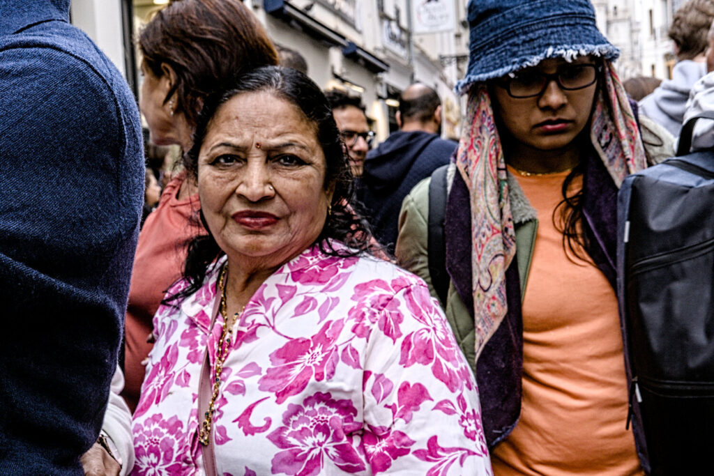 Two individuals standing close together in a crowded urban setting, partially obscured by the ambient environment.